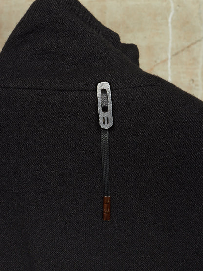 Close-up of a black textured garment featuring a decorative silver metal zipper pull with a dark cord and a small brown wooden accent at the bottom.