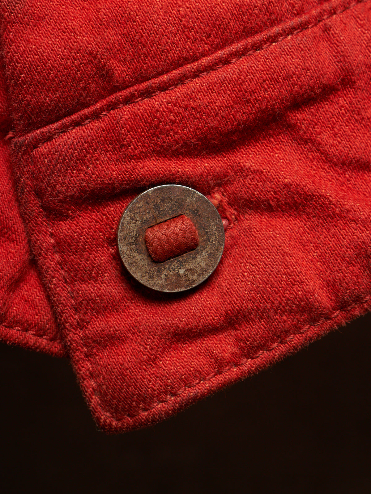 Close-up of a red quilted fabric garment with a round metal button featuring a red center, set against a dark background.