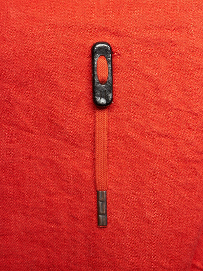 A close-up of a zipper pull with a black metal head and a red-orange zipper tape, shown on a textured red fabric background.