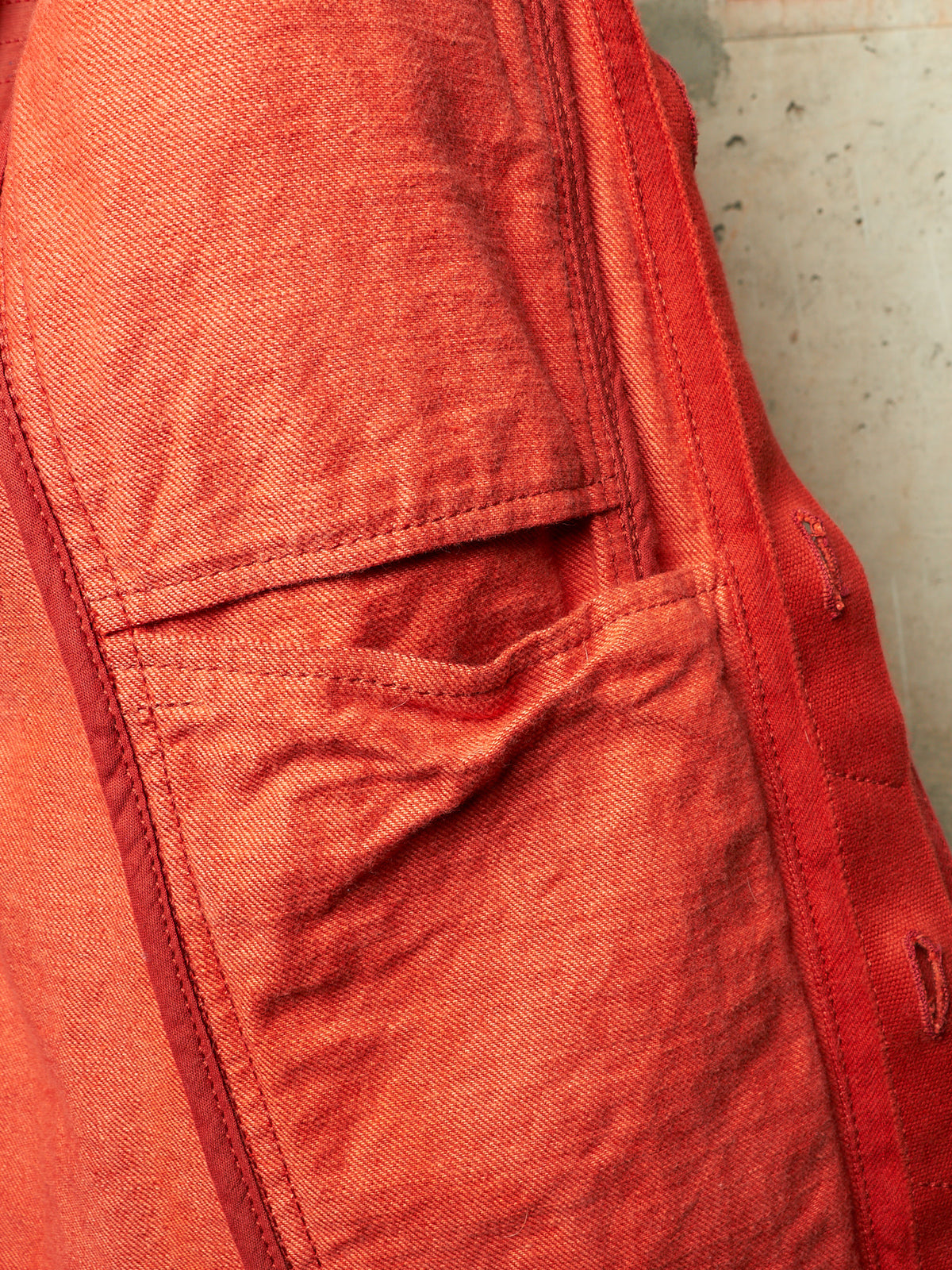 Close-up detail of a red-orange textured fabric garment showing a pocket and stitched seam.