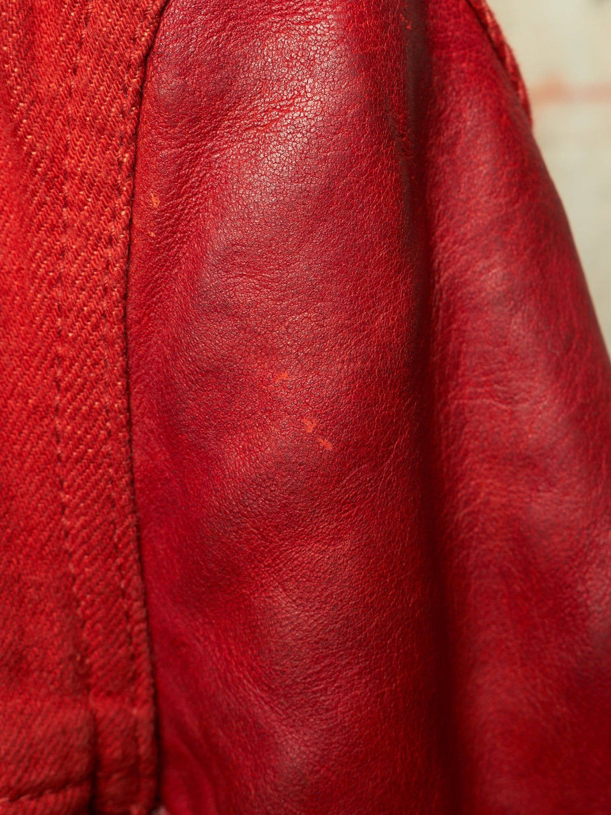 Close-up of a red leather jacket showing the texture of the leather and a portion of the red denim fabric.