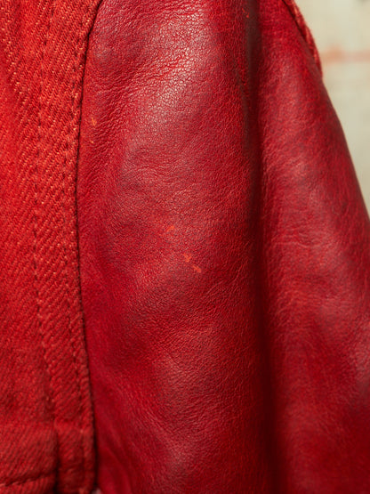 Close-up of a red leather jacket showing the texture of the leather and a portion of the red denim fabric.