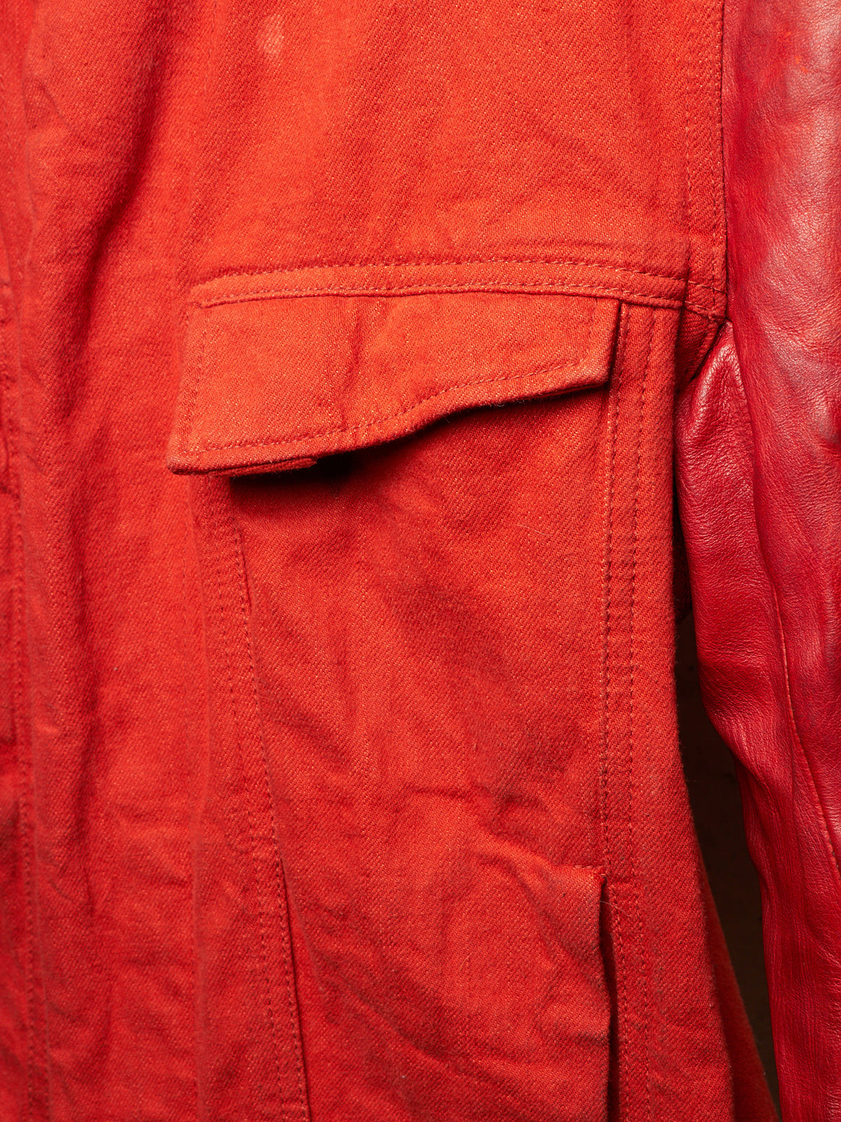 Close-up detail of a red jacket showing a textured canvas flap pocket and smooth leather sleeve.