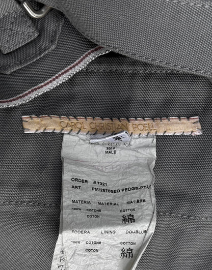 A close-up of a clothing label for Carol Christian Poell’s 2010 “IN-BETWEEN” PM/2578 PEDGE self-edge high-waisted metre pants, showing brand and product details on grey fabric—evoking avant-garde fashion sensibilities.
