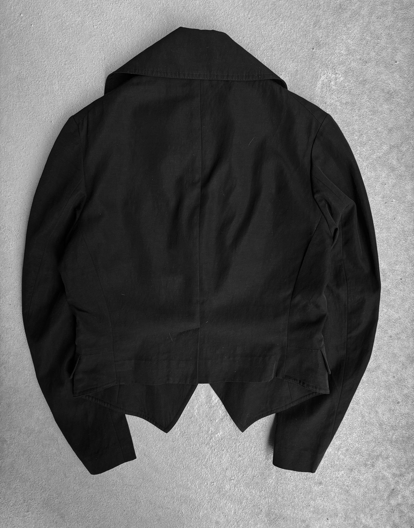 The Y’s by Yohji Yamamoto SS07 Cropped Cotton-blend Blazer, a black long-sleeved piece with a wide collar and asymmetrical hem, is shown laid flat back-side up on a gray surface—an eye-catching work by Yohji Yamamoto.