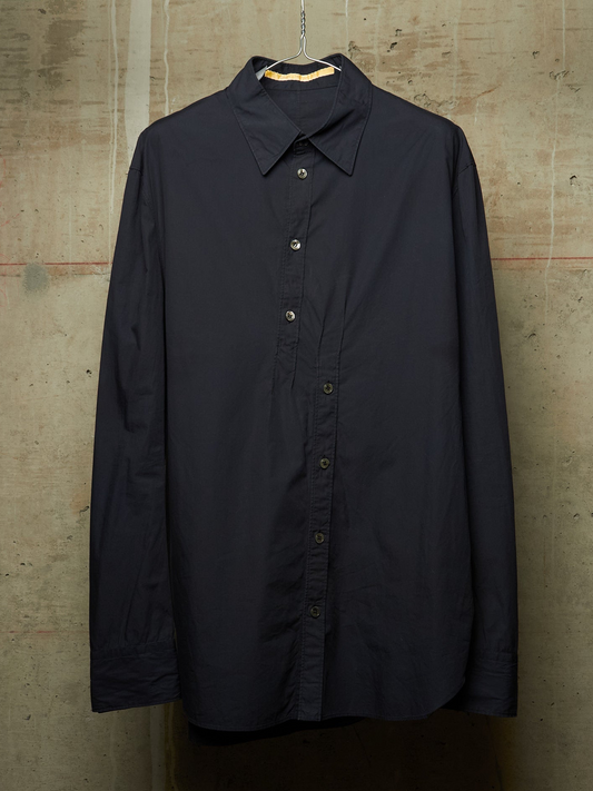 A dark navy blue long-sleeve button-up shirt hanging on a metal hanger against a textured concrete wall.