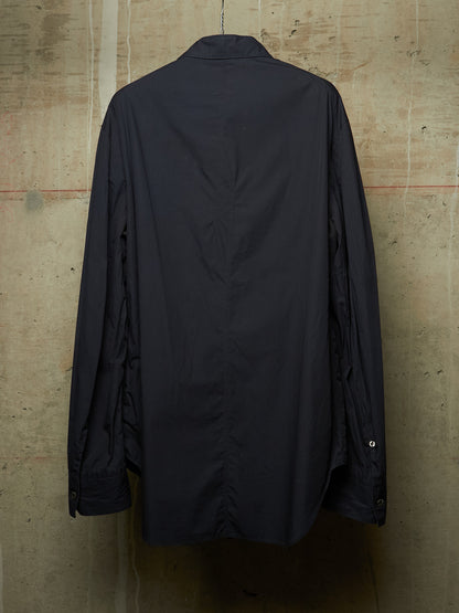 A dark navy blue long-sleeve button-up shirt shown from the back, hanging against a textured concrete wall.