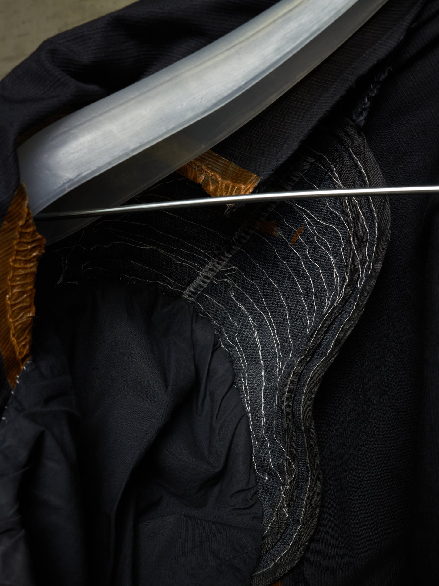 Close-up detail of a black garment with contrast white stitching, a metallic silver curved trim, and a gold inner lining.