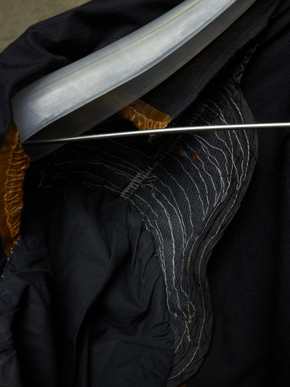 Close-up detail of a black garment with contrast white stitching, a metallic silver curved trim, and a gold inner lining.