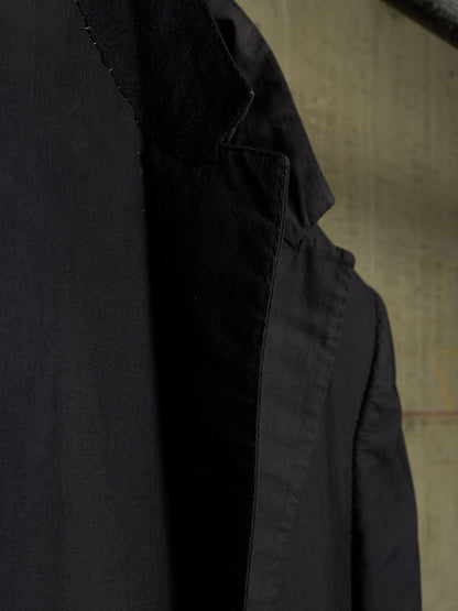 Close-up detail shot of a black jacket, showing the texture of the fabric and the inner lining, set against a neutral textured background.