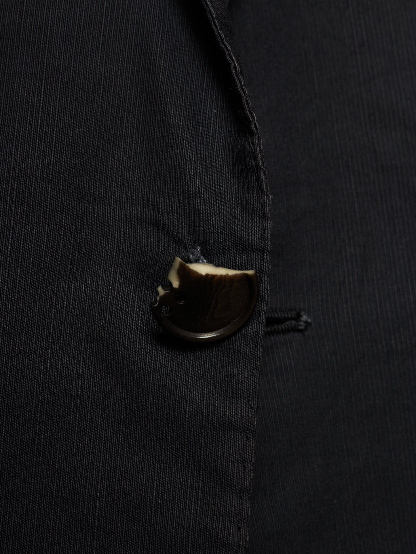 Close-up of a black pinstriped jacket or blazer with a dark brown button.