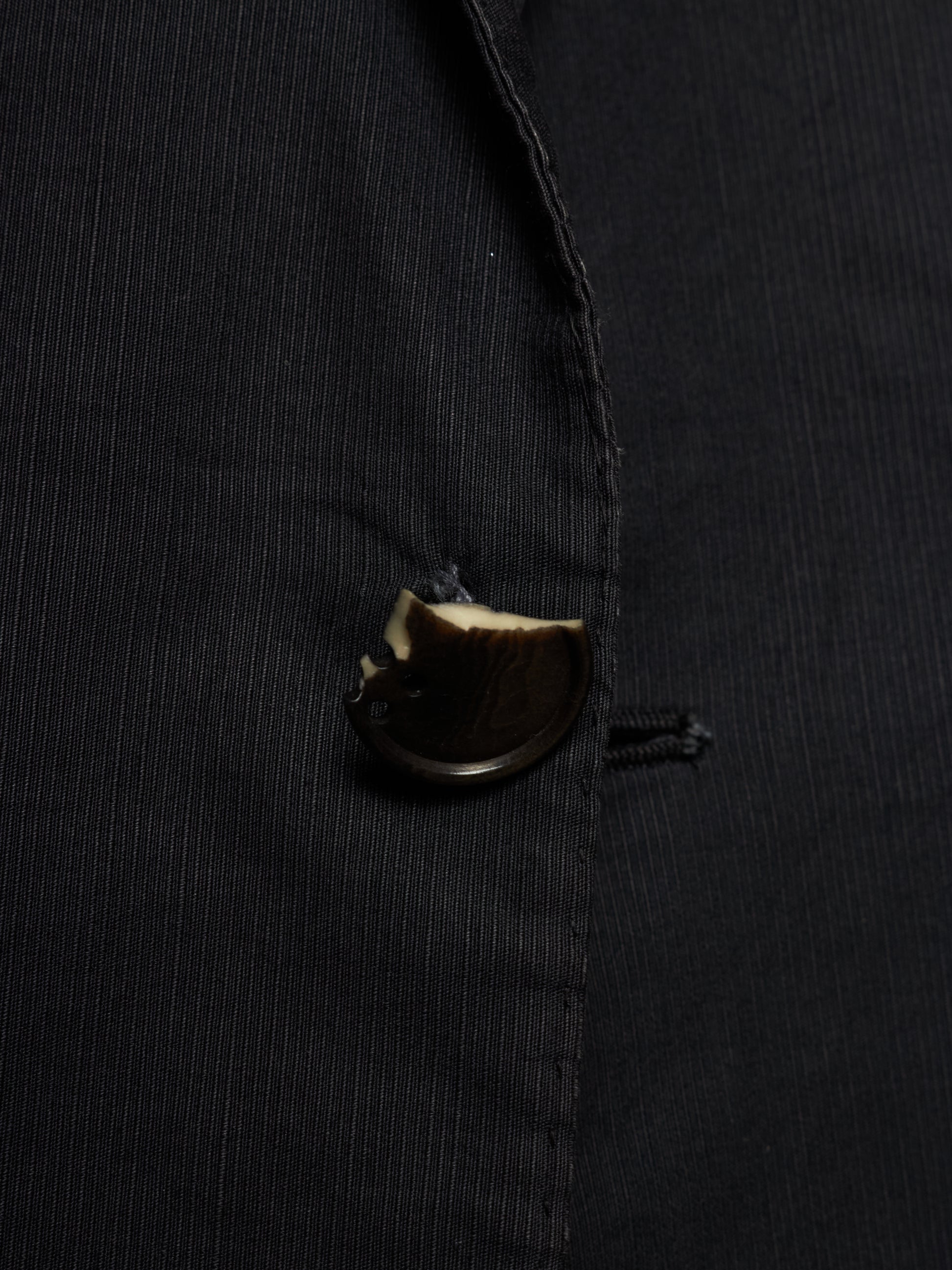 Close-up of a black pinstriped jacket or blazer with a dark brown button.