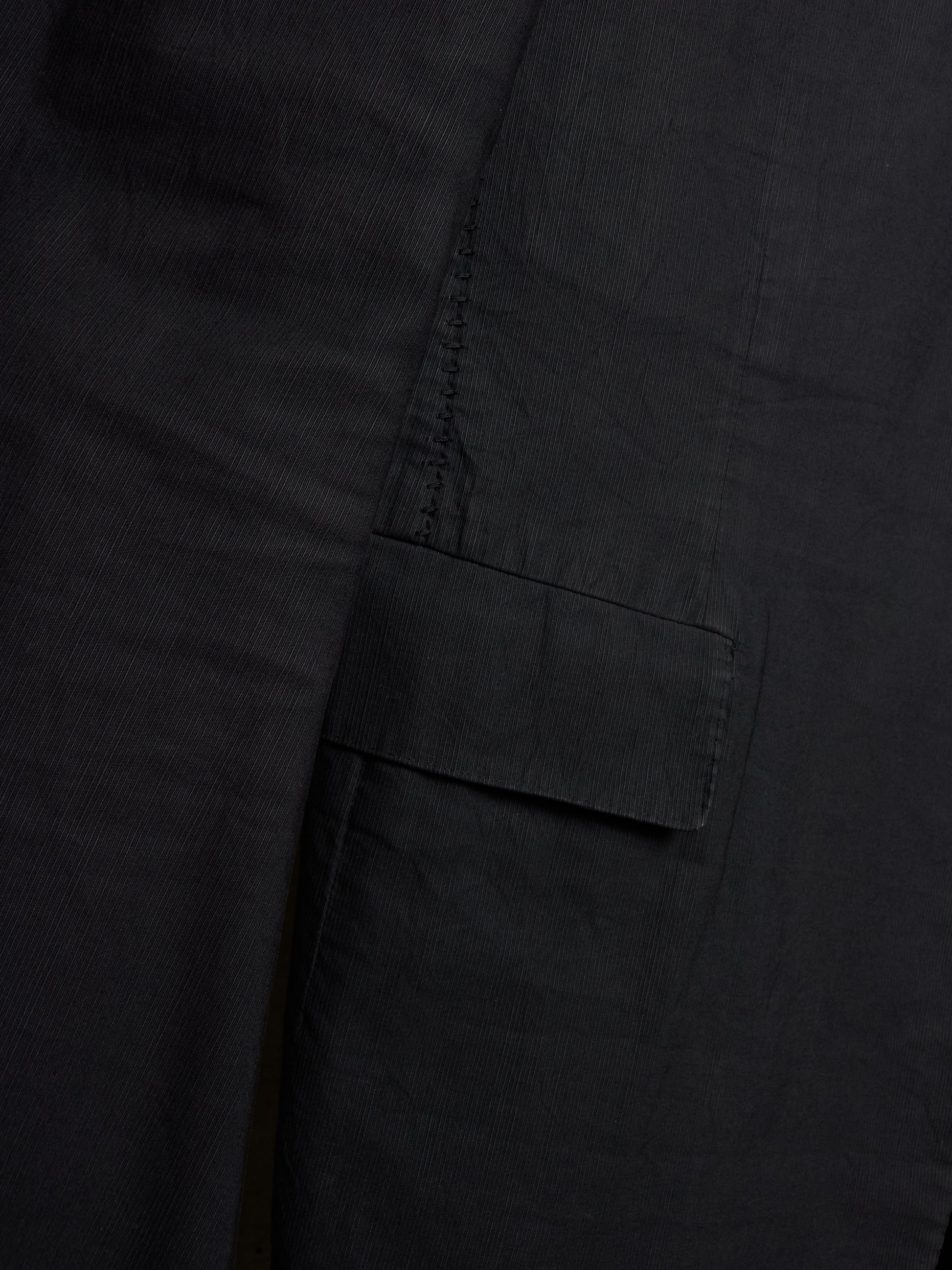 Close-up detail of a black fabric garment showing a side pocket with a flap tab and dark contrast stitching.