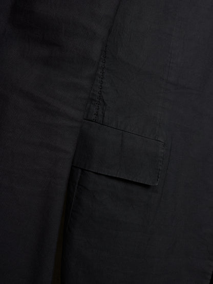 Close-up detail of a black fabric garment showing a side pocket with a flap tab and dark contrast stitching.