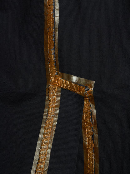 Close-up of a black garment featuring a prominent metallic gold and silver embroidered border detail.