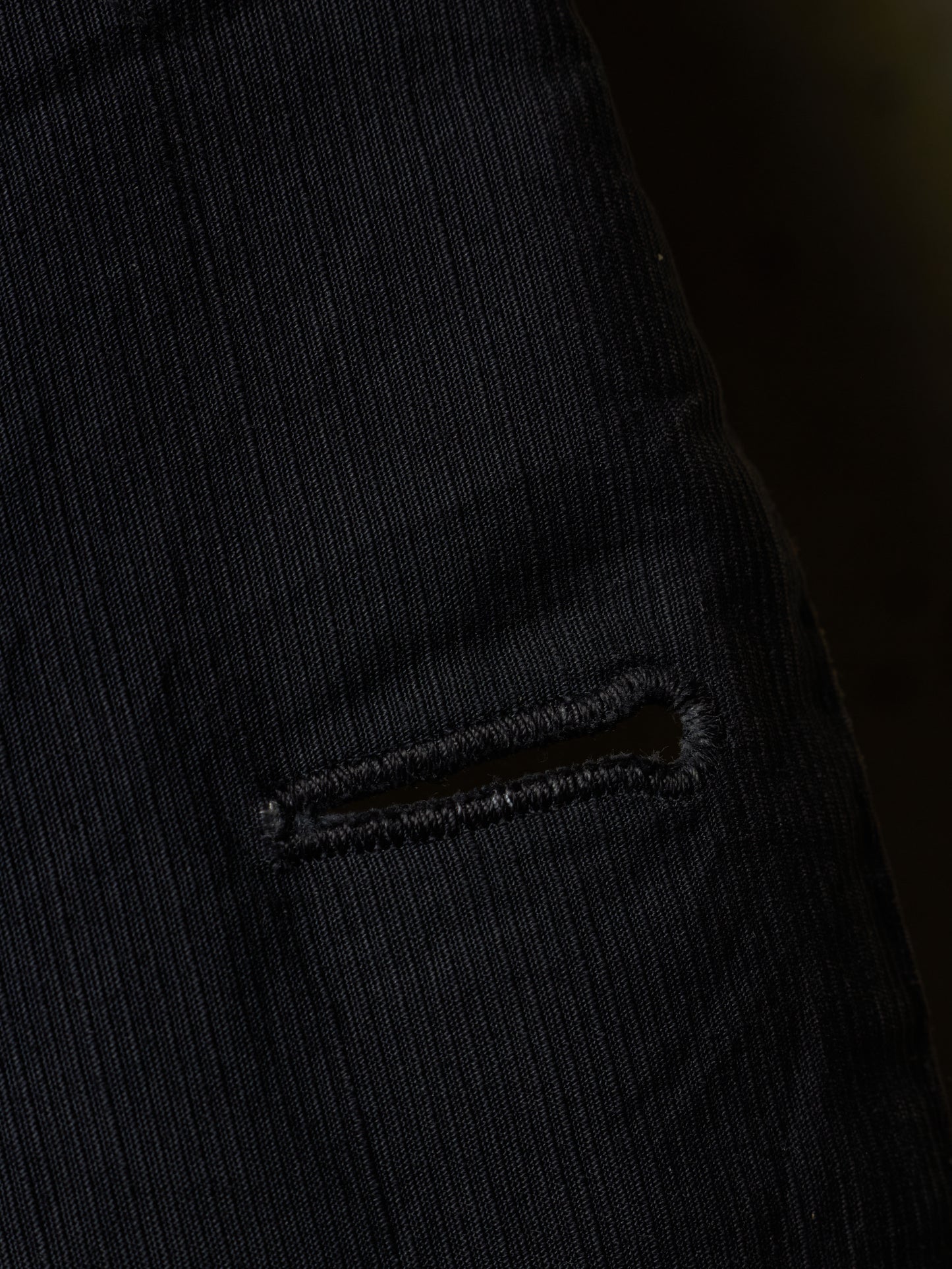 Close-up of a black ribbed corduroy fabric with a small horizontal slit detail.