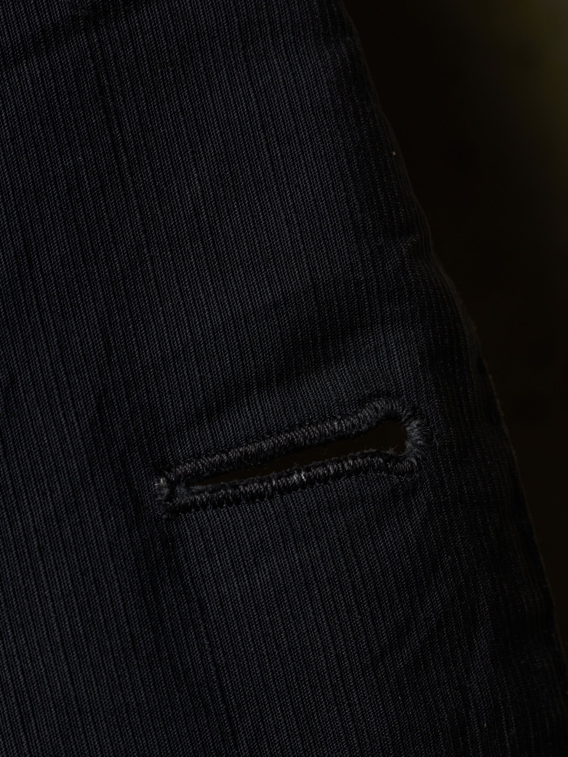 Close-up of a black ribbed corduroy fabric with a small horizontal slit detail.