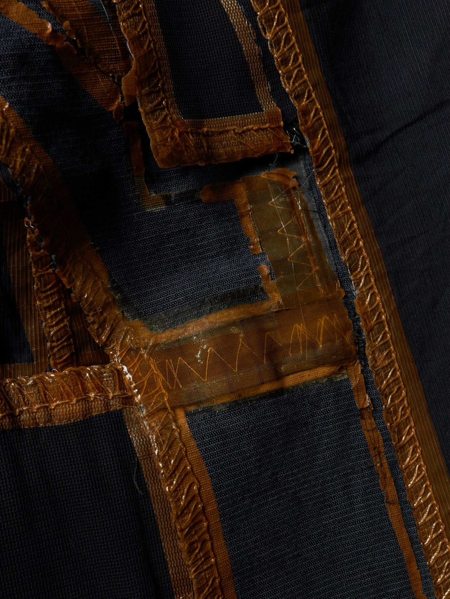 Close-up detail of a dark navy or black textile garment featuring prominent metallic gold embroidered trim and geometric stitched patterns.