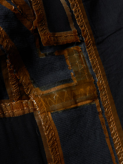 Close-up detail of a dark navy or black textile garment featuring prominent metallic gold embroidered trim and geometric stitched patterns.