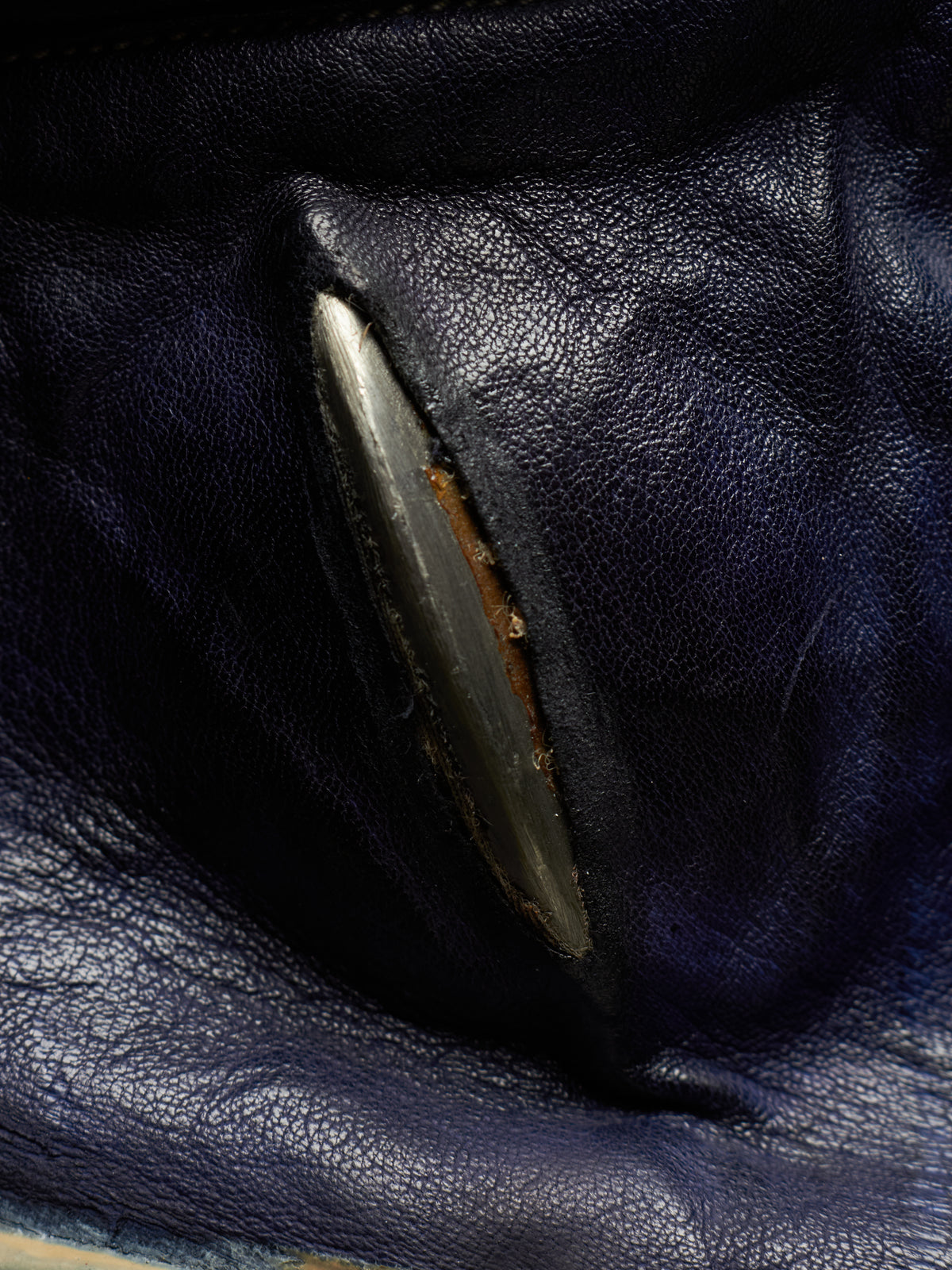 Close-up of a dark navy blue leather item showing a worn, chipped, and rusted edge on a metallic silver-colored component.