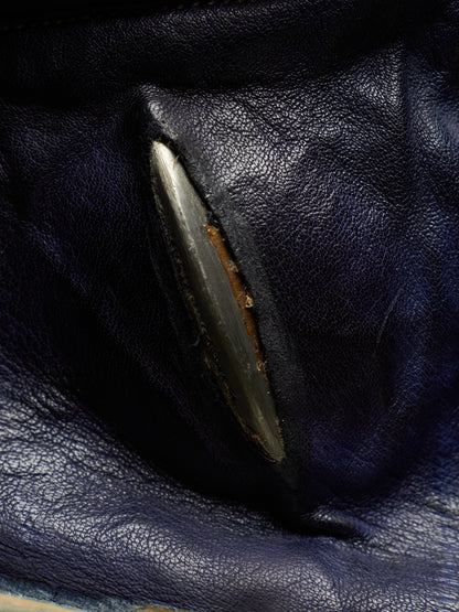 Close-up of a dark navy blue leather item showing a worn, chipped, and rusted edge on a metallic silver-colored component.