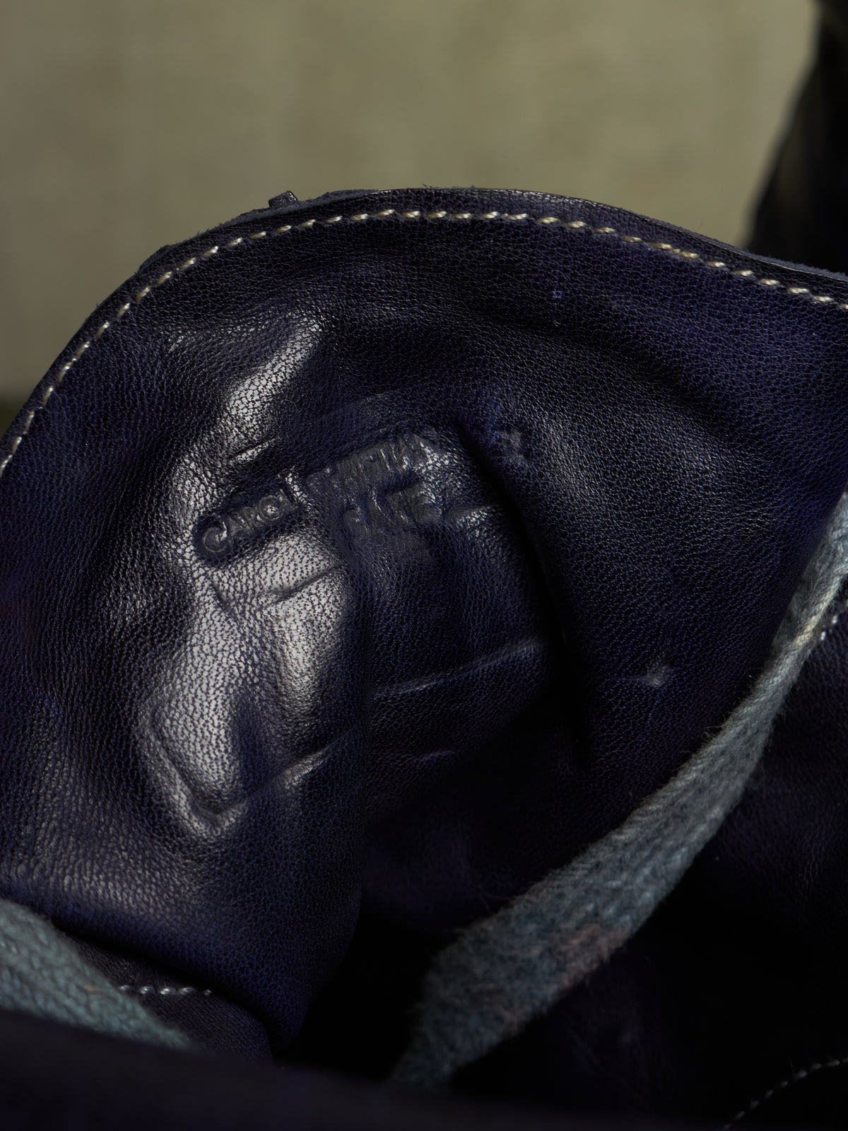 Close-up of the interior lining of a dark navy leather bag or boot, showing pebbled leather texture, white stitching, and an embossed logo that appears to read 'Crazy Dog'.
