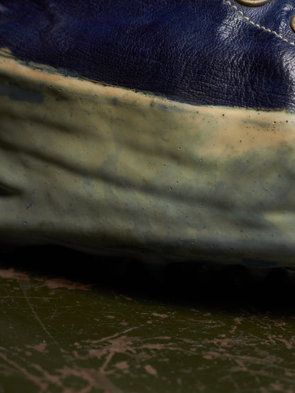 Close-up of a worn blue leather shoe with a heavily scuffed, dirty off-white rubber sole resting on a scratched dark green surface.