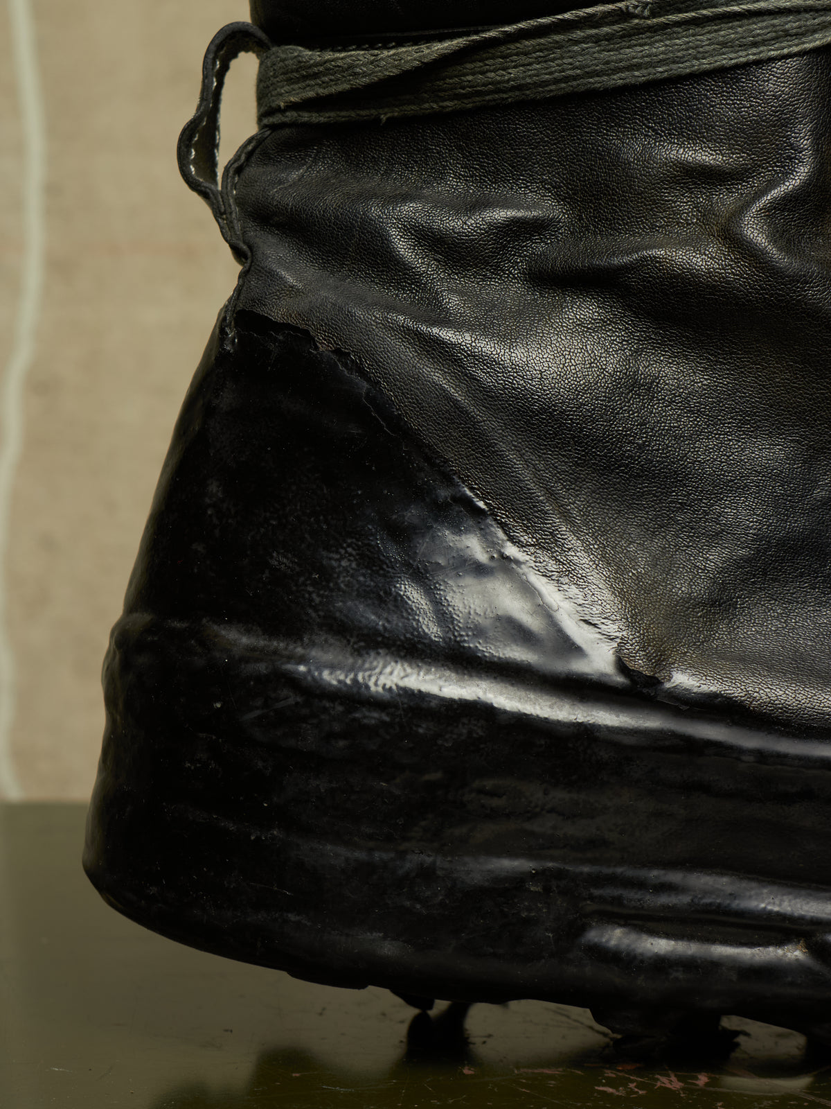 Close-up of a black leather boot with a glossy finish, showing the side and heel area against a neutral background.