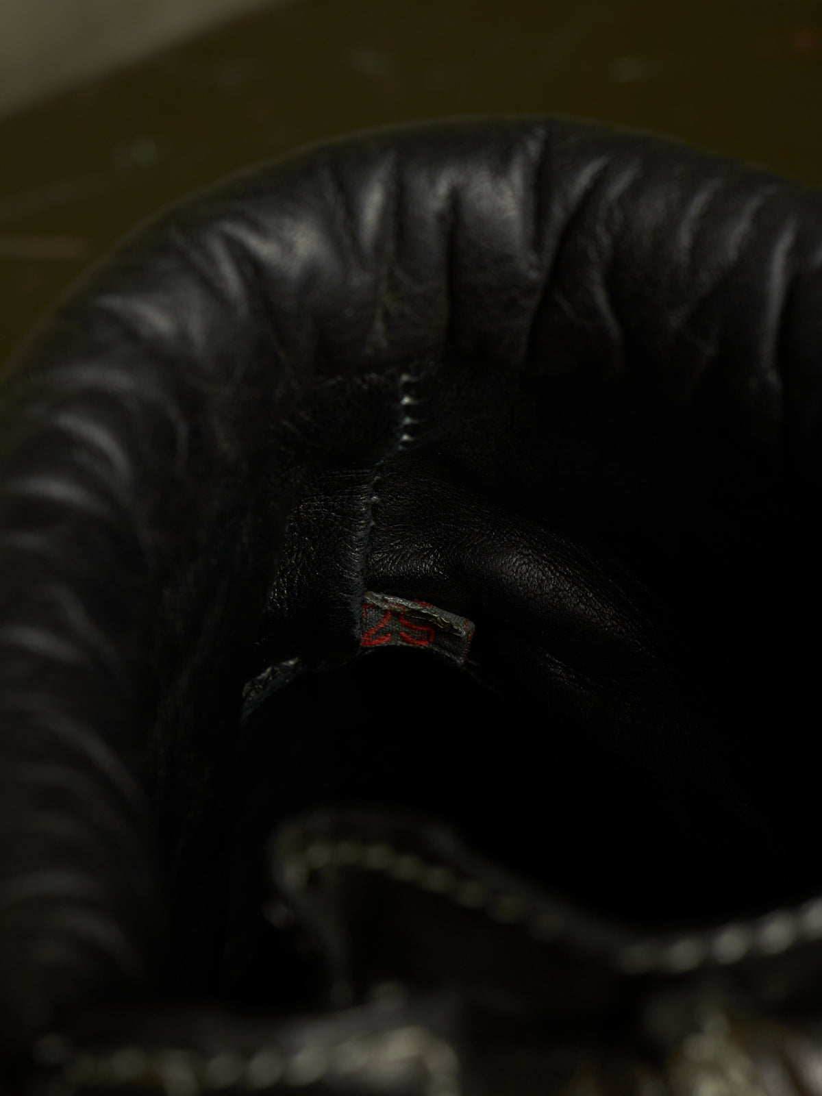 Close-up of the inside of a black leather boot or shoe, showing the interior lining, stitching, and a small red-and-white brand tag near the opening.