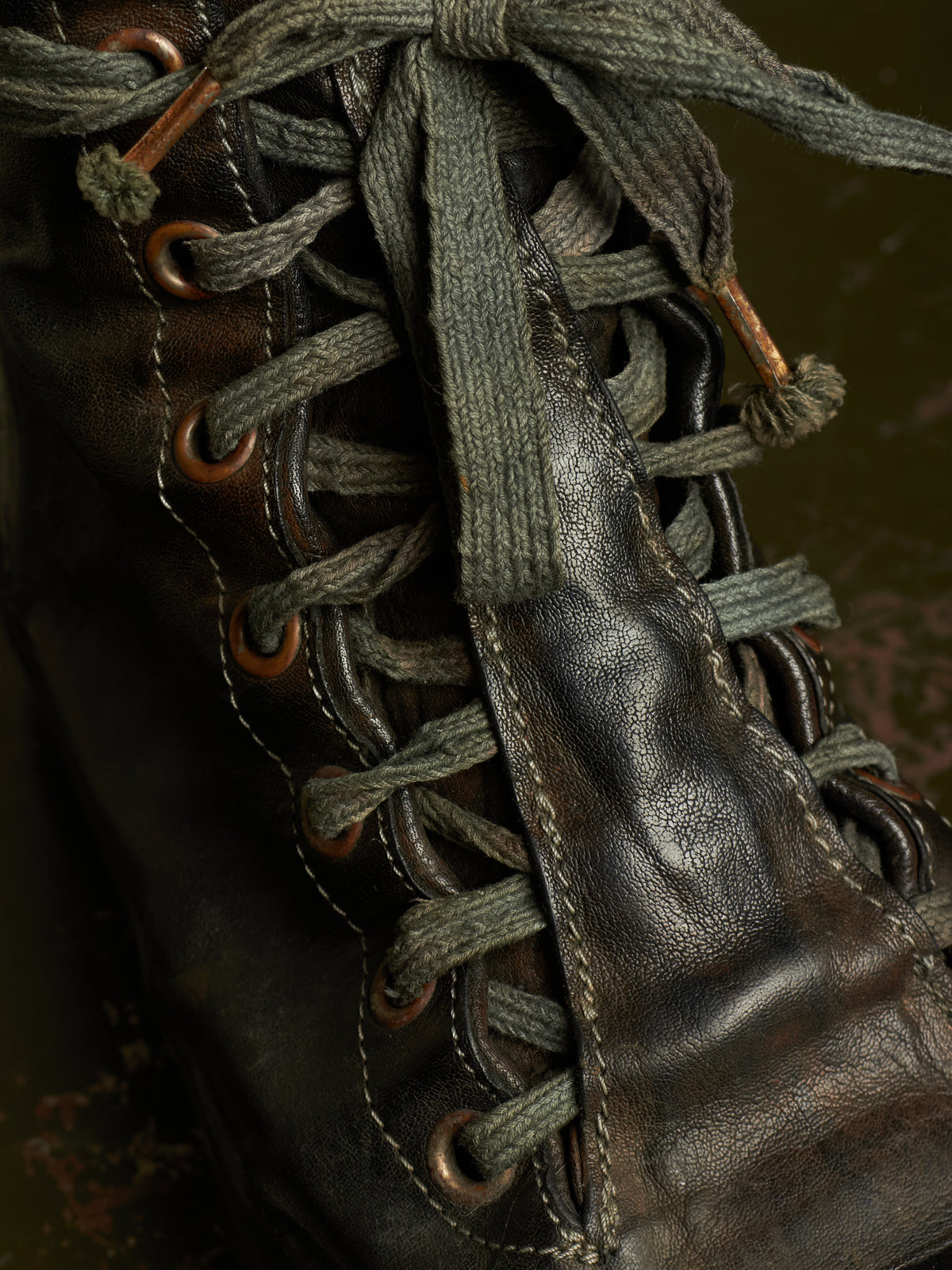 Close-up of a dark brown leather lace-up boot with thick textured gray-green laces threaded through copper-toned eyelets.
