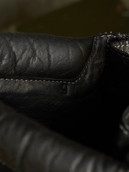 Close-up detail of a black leather item showing the texture, stitching, and a zipper edge.