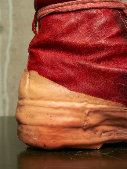 A close-up of a red leather boot or shoe sole and upper section, showing a thick textured tan rubber sole and a red leather upper with a matching red laces.