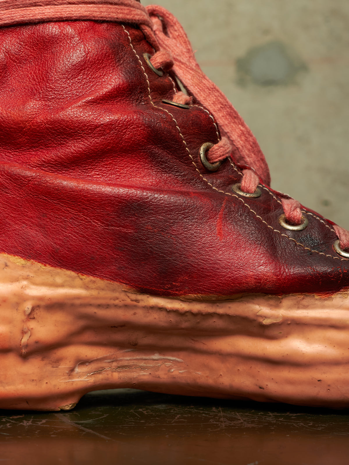 A close-up of a red leather lace-up boot with a thick, sculpted, organic-shaped tan sole.