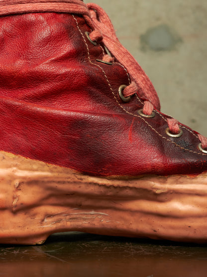 A close-up of a red leather lace-up boot with a thick, sculpted, organic-shaped tan sole.