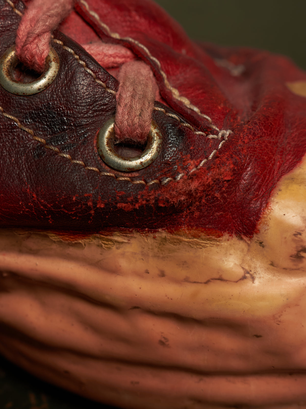 Close-up of a red leather baseball glove with pink laces and metal eyelets, resting on a textured tan surface.
