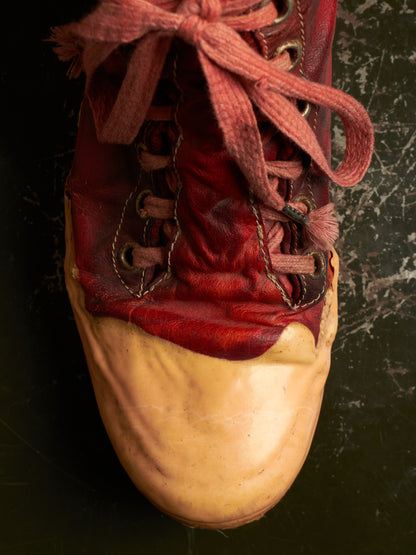A close-up of a vintage high-top sneaker with a distressed red leather upper, matching red laces, and a tan rubber toe cap, set against a dark textured background.