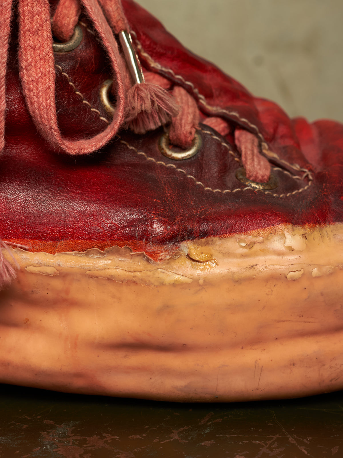 A close-up of a red leather sneaker with matching red laces and a thick tan sole, photographed against a neutral beige background.
