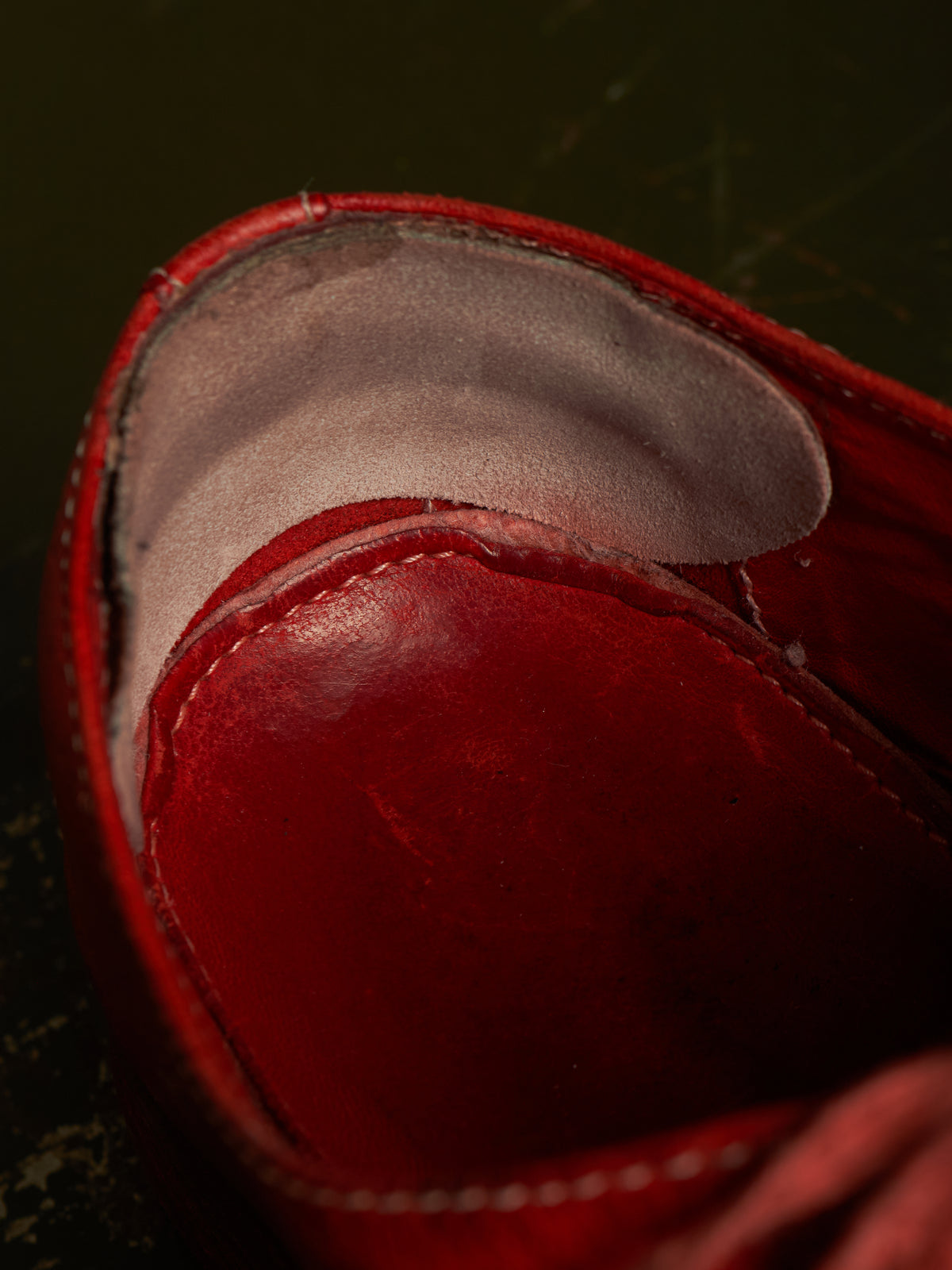Close-up of a red leather shoe interior showing the red footbed and light gray lining against a dark background.