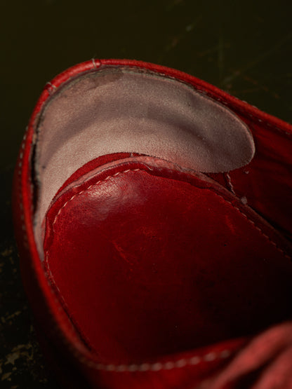 Close-up of a red leather shoe interior showing the red footbed and light gray lining against a dark background.