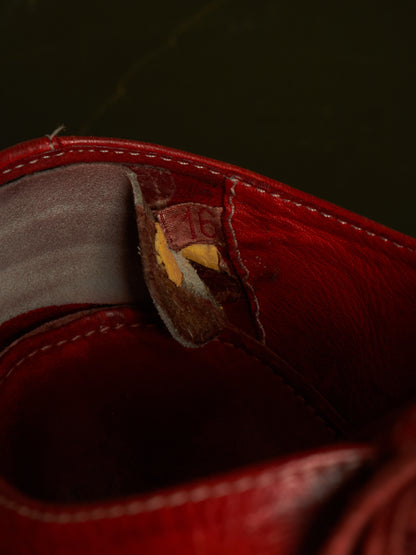 Close-up of a red leather boot or shoe interior showing a worn pull tab with exposed yellow material and visible stitching.
