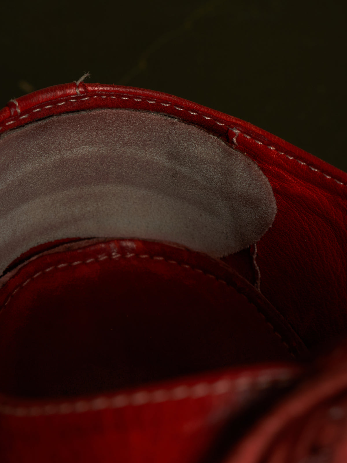 Close-up detail of a red leather shoe or boot interior, showing the red leather lining with white stitching and a gray suede or fabric insole.