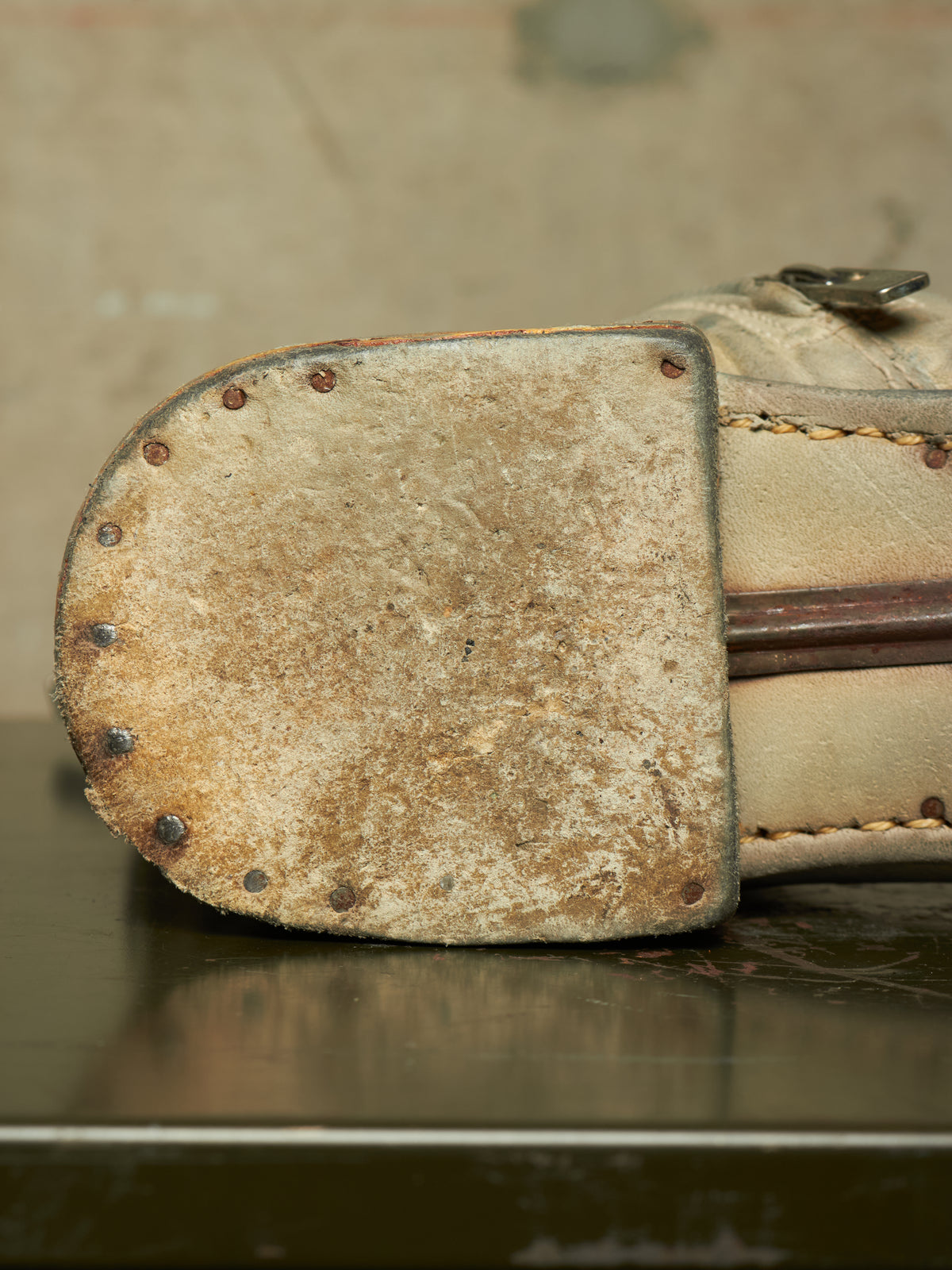 A close-up of a worn beige leather boot sole with metal rivets, showing significant scuffing and dirt, resting on a dark reflective surface.