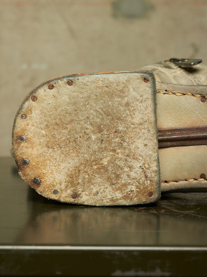 A close-up of a worn beige leather boot sole with metal rivets, showing significant scuffing and dirt, resting on a dark reflective surface.