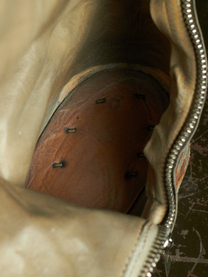 Close-up of the interior of a beige leather bag or case, showing a brown wooden insert or shoebox-like panel with several small black pins attached, and a silver zipper running along the right side.