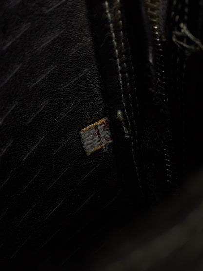 Close-up of a black textured leather bag showing a small fabric brand tag with the number 13 and dark metal zipper.