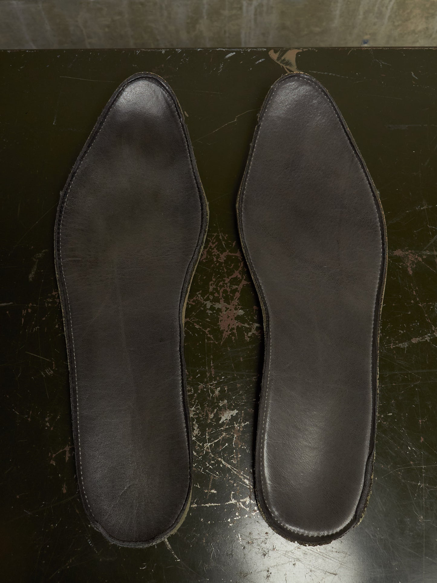 A pair of dark brown leather insoles laid flat on a dark, worn surface.