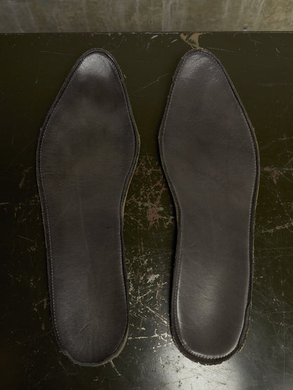A pair of dark brown leather insoles laid flat on a dark, worn surface.