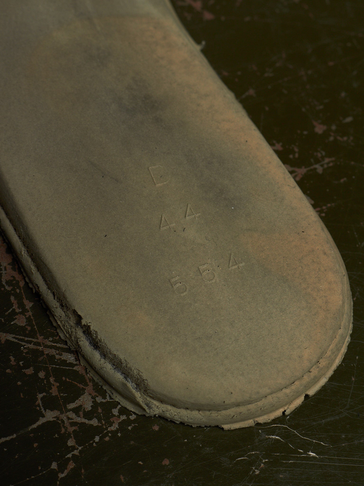 A close-up of a worn, dusty gray shoe sole with embossed size markings '4 4 5 5 4', resting on a dark, scratched surface.