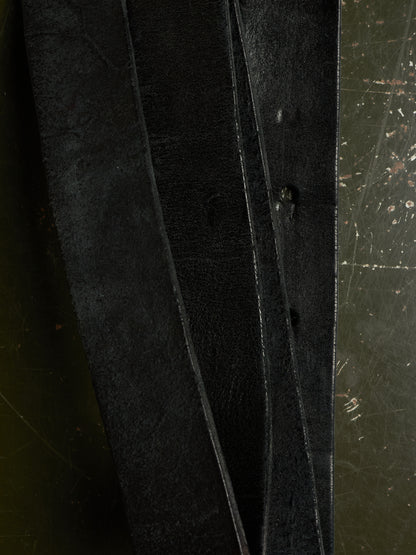 A close-up of three dark, textured leather strips or straps laid vertically against a dark, scratched metal surface.