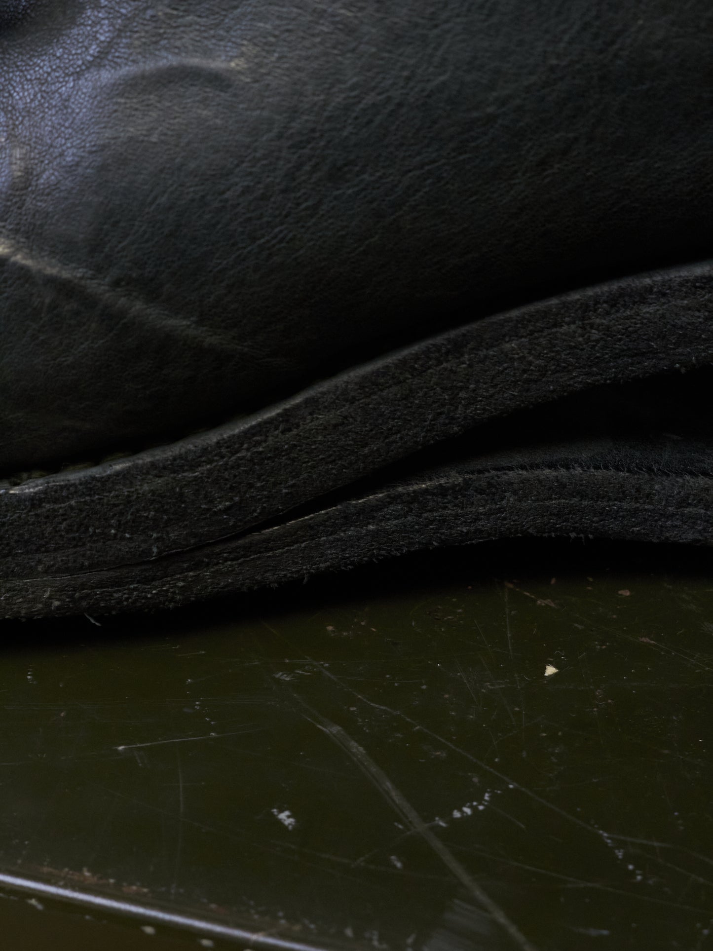 Close-up detail of a black leather or faux-leather item, showing layered edges and a dark reflective surface below.